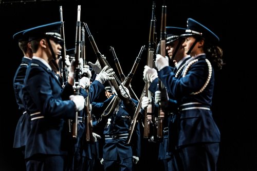 Group of people dressed in military holding rifles in a ceremonious formation standing in a circle