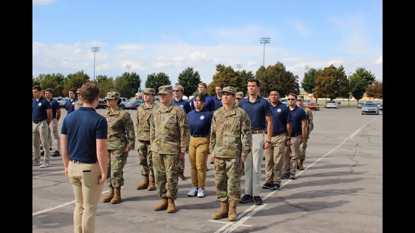 Group of men and women in camo and tan khakis and blue polos standing in formation