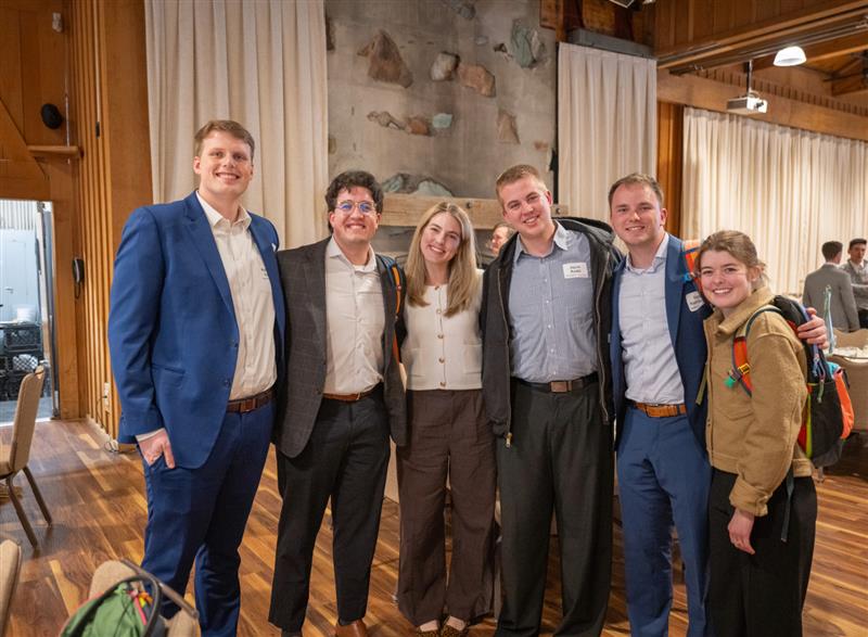 Six students stand for a photo together inside a wooden lodge at a conference.