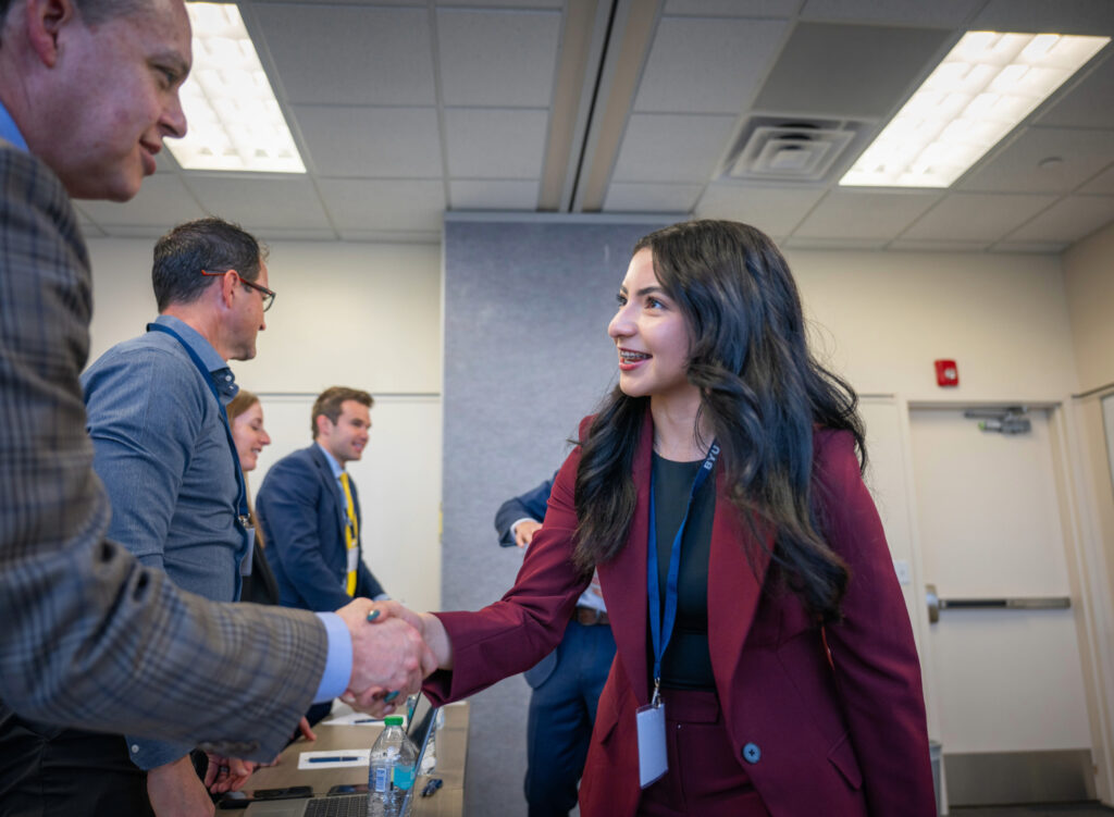 A woman in a maroon blazer shakes a man's hand.