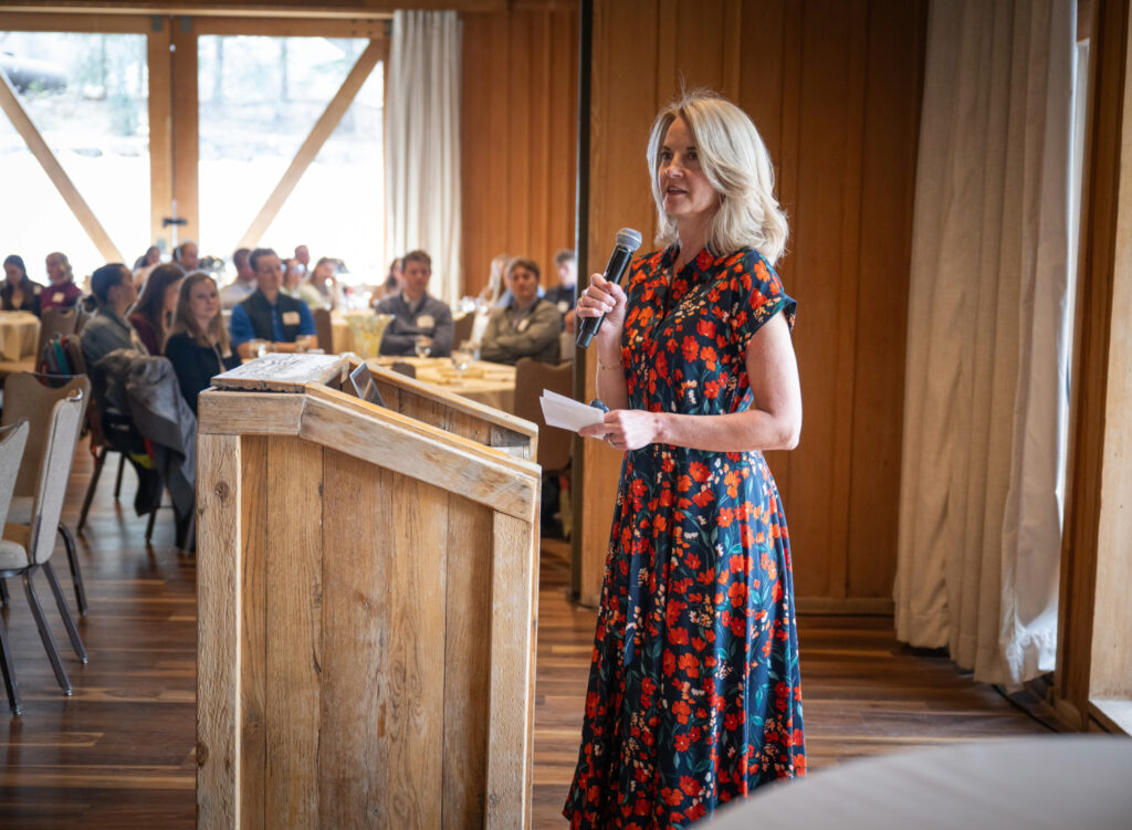 A woman in a red and blue dress talks at a wooden podium.