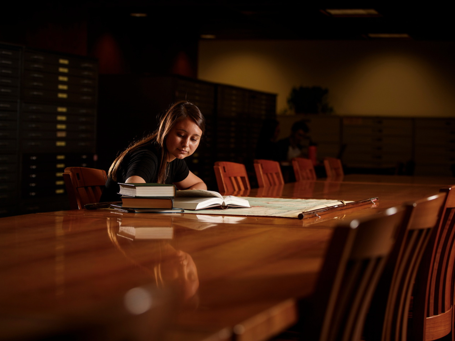 A student studies at a large desk in a dimly lit room.