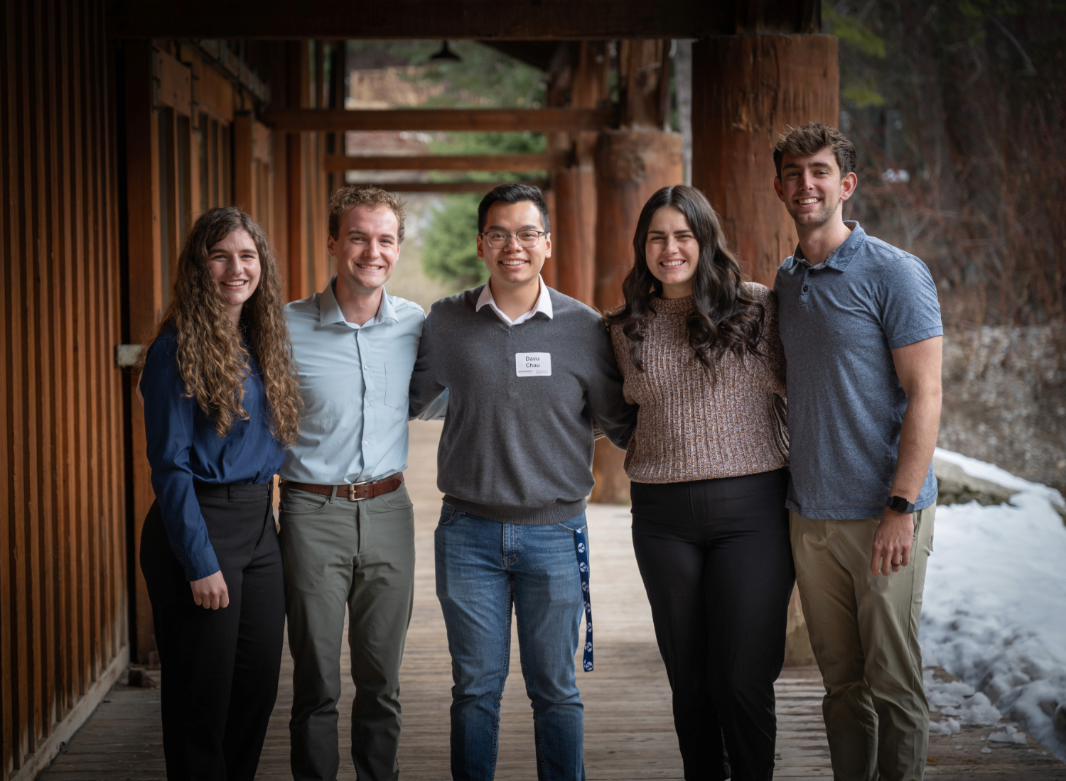 Five students stand together outside a wooden lodge.