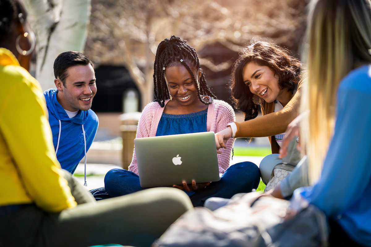 Group of diverse students sitting on the lawn looking at a computer