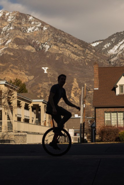 Isaac Pettit, a white male, riding a red unicycle in front of the mountains.