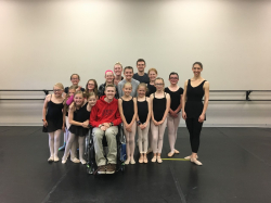Josh Hinton, a white male in a wheelchair, surrounded by young students in ballet uniforms.