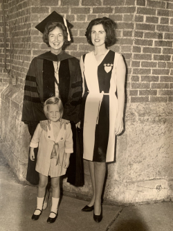 Sue Mika as a child standing in front of her mother, Lynn Keenan, and her grandmother, Lenore Romney. Lenore is in a graduation cap and gown.