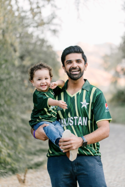 Omer Malik and his son standing outside; Both are wearing matching green soccer jerseys.