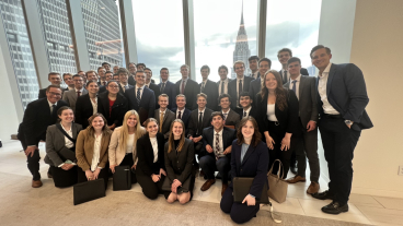 Ian Wright stands with a group of professionally dressed finance students in New York City with the Empire State Building in the background.