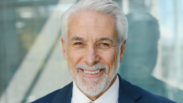 A cleanly dressed older man in a suit with neat gray hair and a beard smiling into the camera.