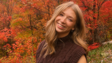 Lindberg smiles at the camera from the side of a mountain. The background is filled with wildflowers and bright orange autumn leaves.