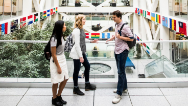 Three students stand talking in the atrium of the Tanner Building on BYU campus