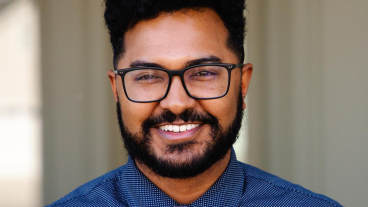 Man wearing collared blue shirt and black-rimmed glasses smiles for headshot photo.