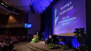 Man in a suit stands at a podium and speaks to a large audience