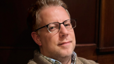 Professional photo of Andersen with his arms crossed and a wooden background.