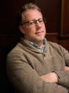 Professional photo of Andersen with his arms crossed and a wooden background.