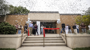 People standing in front of a building with a red ribbon and confetti in the air