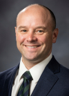 Richard Gardner smiles at the camera in a professional headshot with a gray background.