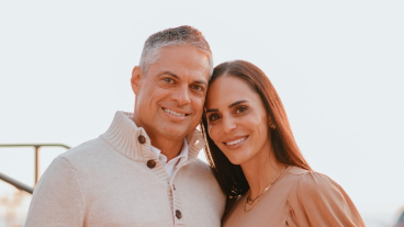 Tyler and Jerriann Banks stand together in the soft golden glow just before sunset. They're both smiling at the camera with one hand in their pockets and the other around each other.