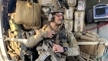 Cameron Strawn sits inside an aircraft in his military gear in front of an array of categorized medical supplies.