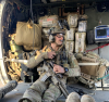 Cameron Strawn sits inside an aircraft in his military gear in front of an array of categorized medical supplies.