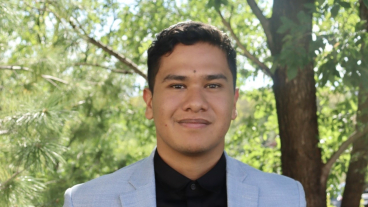 Finance senior Emilio Barrios Ramos poses for a professional photo, dressed in a business suit and standing in front of a tree.