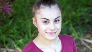 Elaina Greco wears a purple shirt and her hair in a top knot