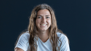 Dressed in a BYU athletic uniform, Folino smiles at the camera as she kneels on a soccer field with a soccer ball.