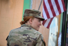 Erin Cole, in army uniform, looks to her right with an American flag draping in the background.