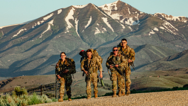 Kate Blaine and three others in army attire are walking with the mountains in the background.