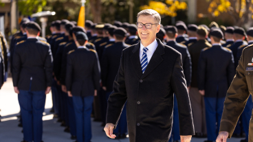 President Lund smiles at the camera with ROTC cadets lined up and facing the background behind him.