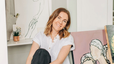 Alexis Belliston sits on the floor in her home surrounded by canvases of her original art.