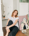 Alexis Belliston sits on the floor in her home surrounded by canvases of her original art.