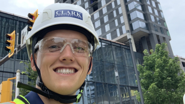 Smith smiles with his hard hat on and standing in front of a building under construction.