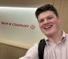 Jonathan Dickson smiles in front of a sign for Bain & Company.