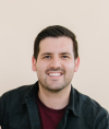 Andres Aleson smiles for a professional headshot wearing a black denim jacket over a dark-red T-shirt.