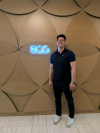 A young man in a polo and vest smiles in front of a glowing BCG sign.