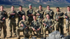 A group of men and women stand in a field. They wear Army uniforms and hold BB guns.