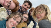 A young family crowds in for a selfie. Pictured are a woman with short blonde hair, a man with a plaid shirt and brown hair, and four children.